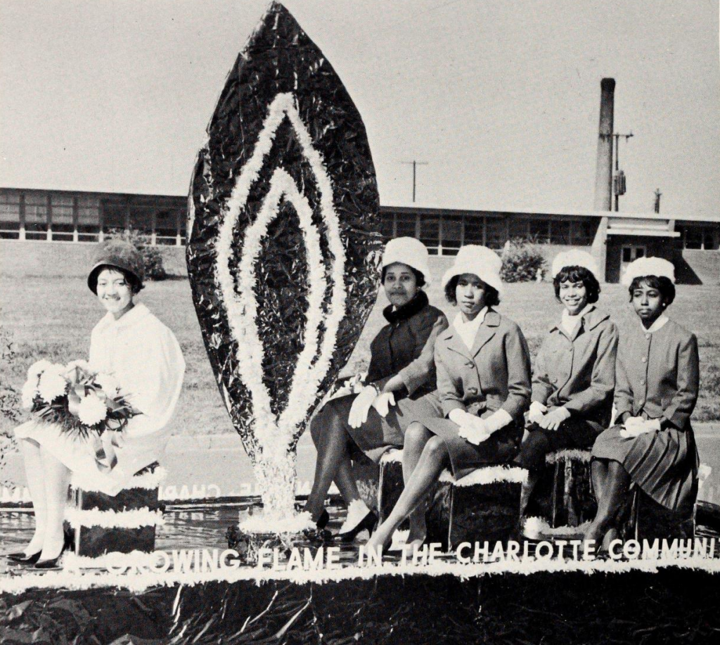 Five women seated on a float that says "A growing flame in the Charlotte Communi[ty]"