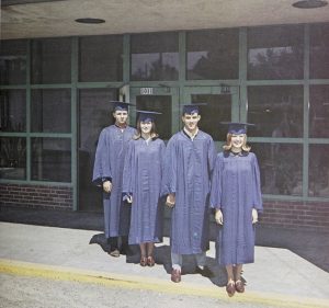 Four graduates in caps and gowns standing in front of a door