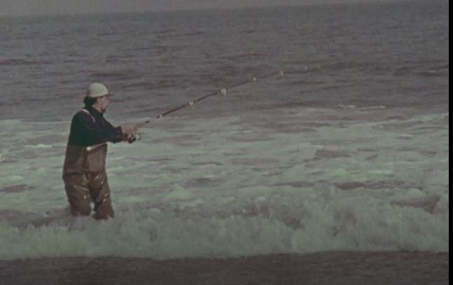 Man standing in the ocean holding a fishing pole