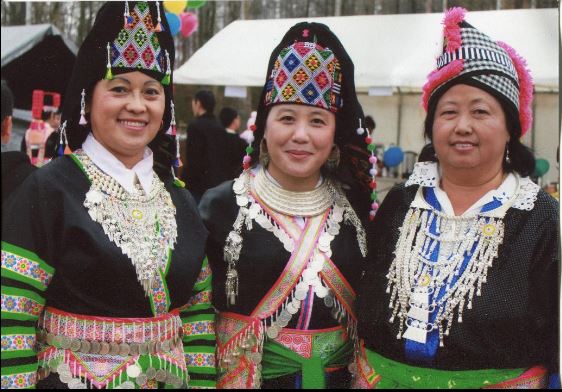 color image of three individuals facing camera and smiling, in traditional Hmong dress