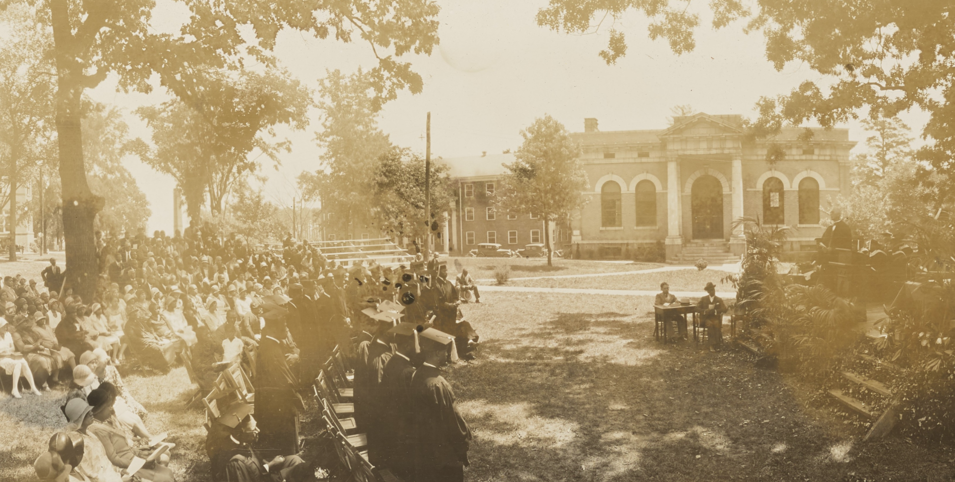 Cropped image of a commencement ceremony at Biddle University in the 1920s. The photo depicts the family and friends watching the commencement speaker. The photo was taken outdoors at Johnson C. Smith University grounds.