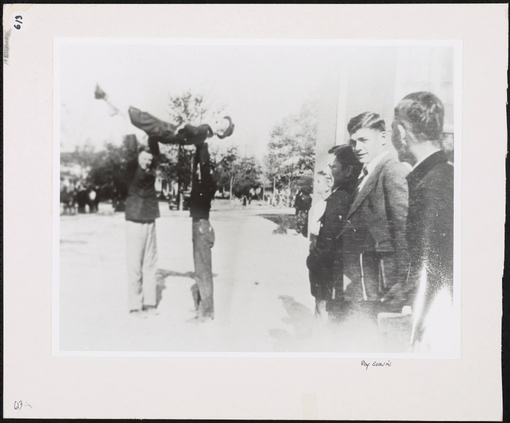 A group of boys watches as two boys lift a third into the air over their heads