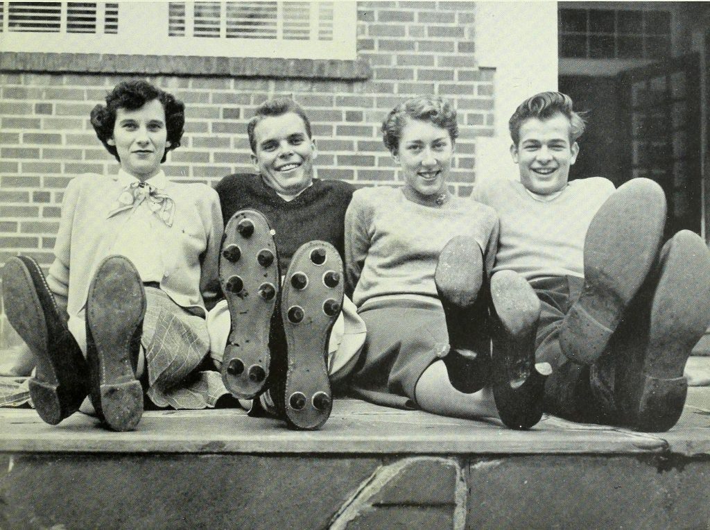 Two men and two women seated on the ground, with their legs crossed at the ankles and feet towards the camera.