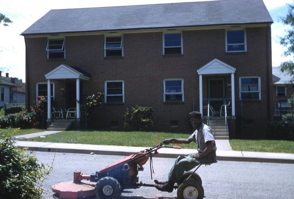 Man on lawn mower in front of homes on Cleveland Ave. Winston Salem