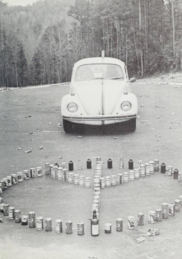 A Volkswagen Beetle is parked behind beer and liquor bottles shaped into a peace sign. 