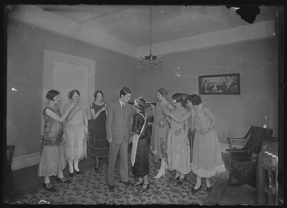 Group of students in dresses pointing at two students, one in a suit and one in a maid costume