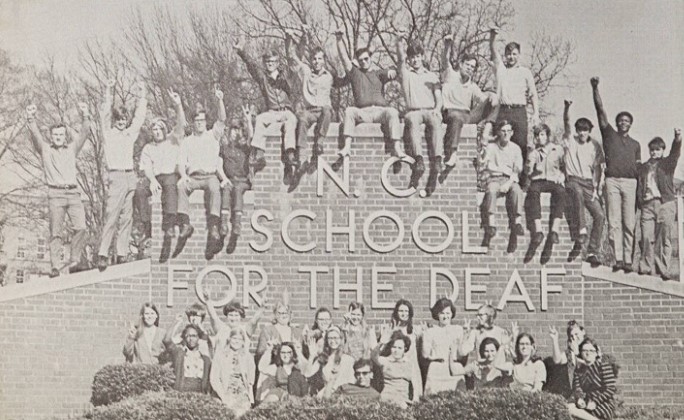 A group of students gather around the brick sign for N.C. School of the Deaf to pose for a photo.