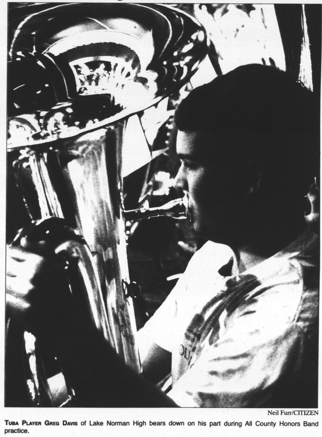 Photograph of a high school student playing the tuba. The caption under the photo reads, "Tuba Player Greg Davis of Lake Norman High bears down on his part during All County Honors Band practice. Photo taken by Neil Furr.