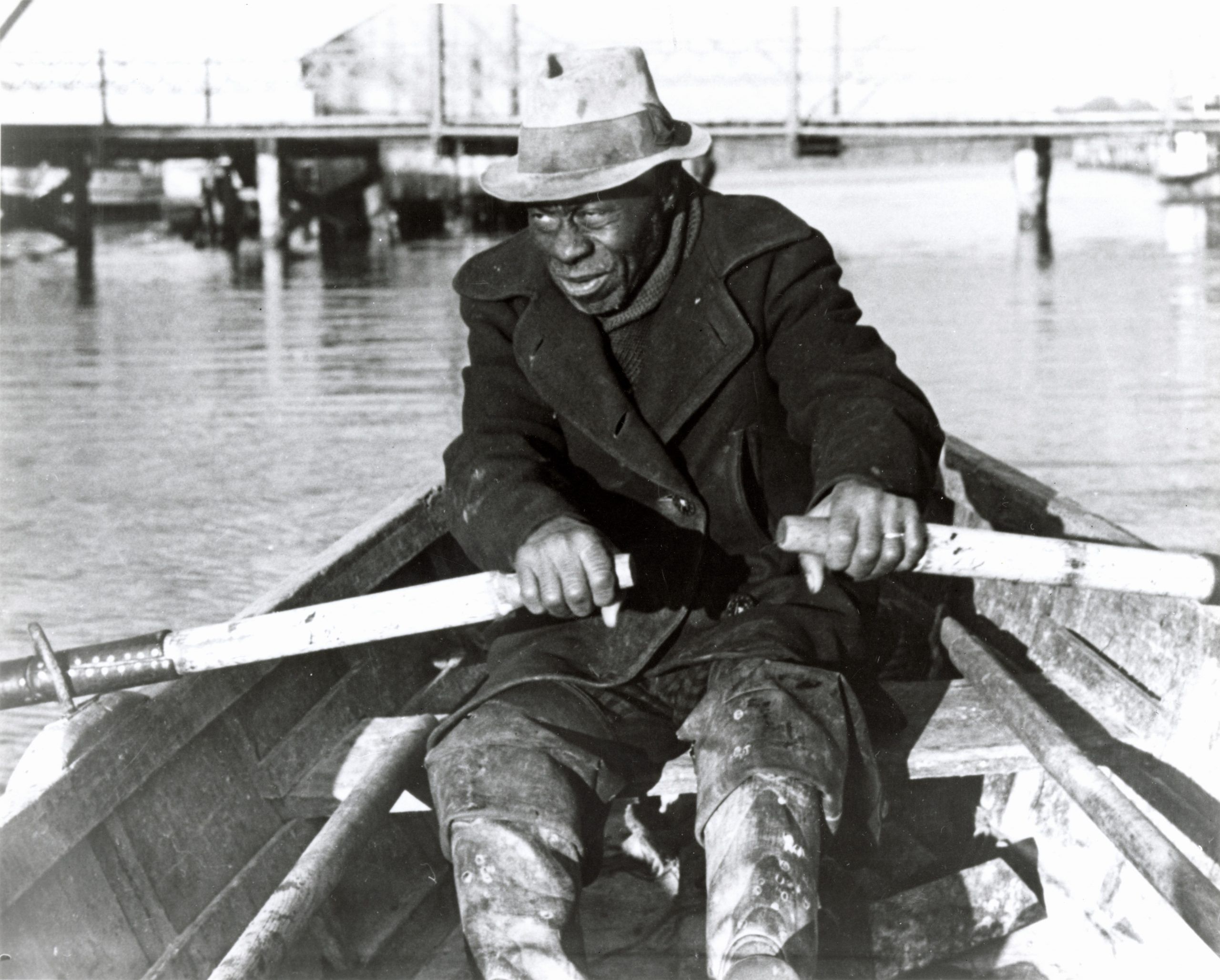 Person with a hat and heavy coat rowing a boat on the Dismal Swamp.
