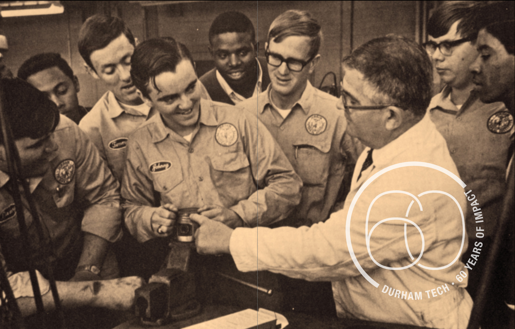 A group of eight male students around a shop tool. One man, with the name tag Johnny is touching the tool and looking at the professor who is talking to the class and also touching the tool.