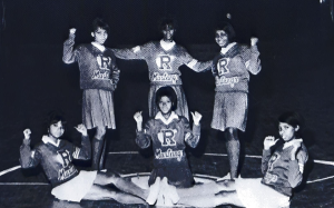 A photo of five cheerleaders; three are standing, and three are seated in front.