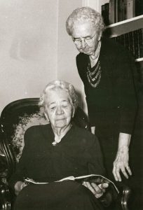 Mary Petty sitting, reading a book, and Annie Petty standing, reading over her shoulder