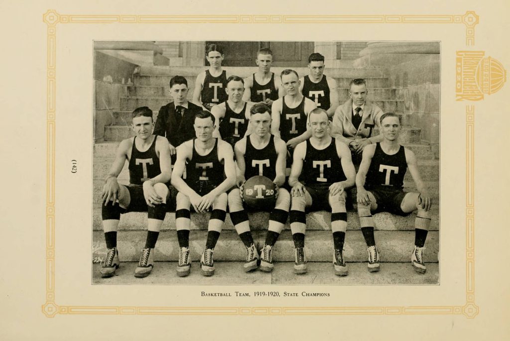 Group of white men posed with a basketball with a "T" logo on their shirts
