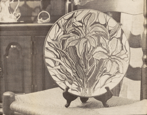 A newspaper clipping of a photo of a ceramic plate. The plate is covered in a floral design.