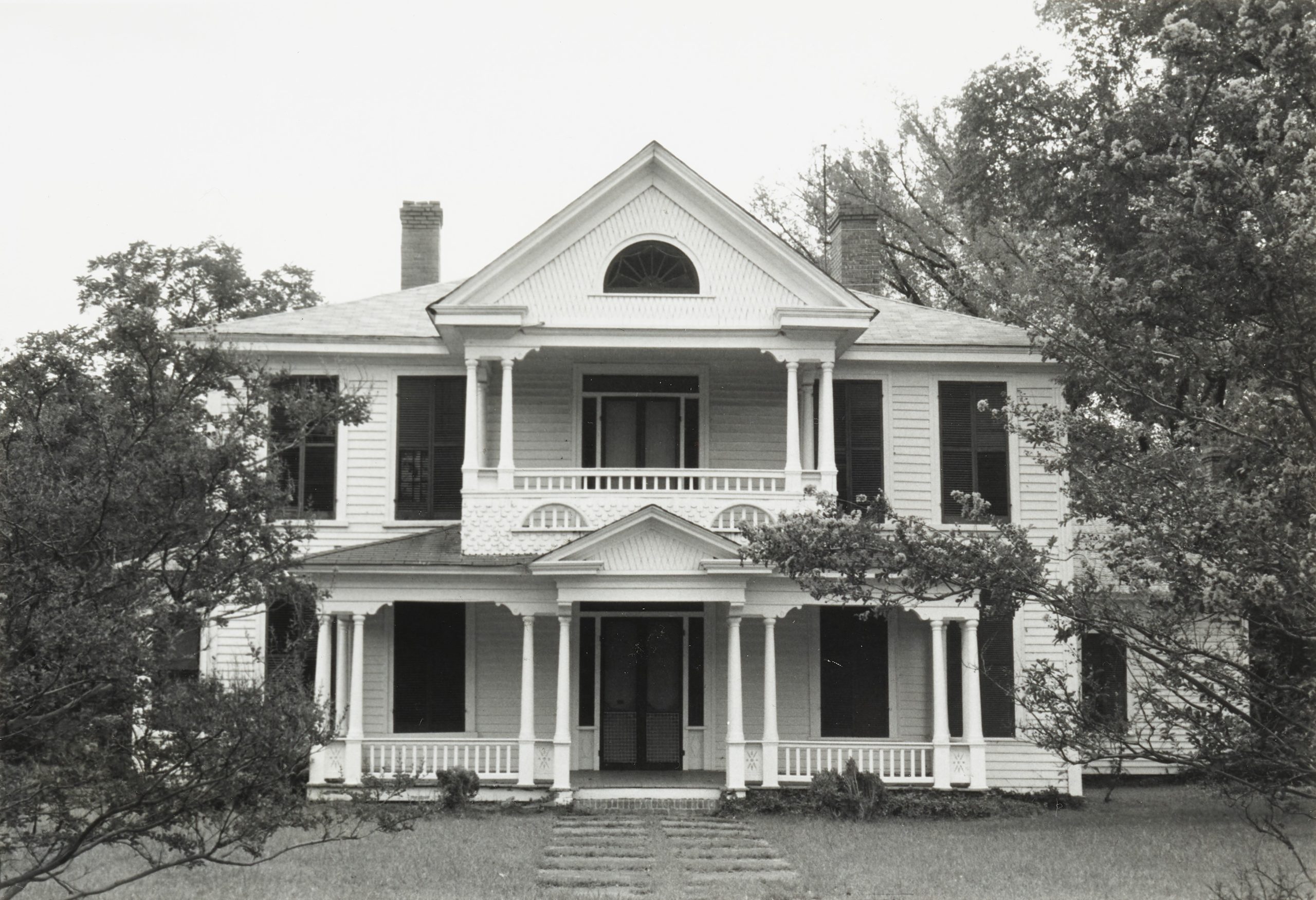 Image of the front of a 19th century two-story home. There is a 2nd floor balcony and a covered front porch.