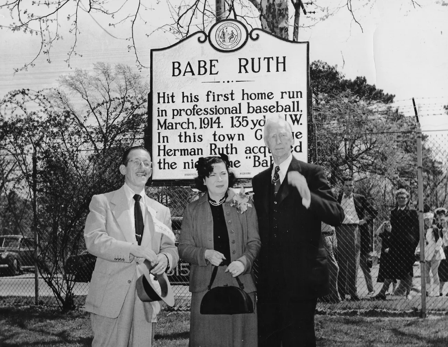 Three people standing in front of the sign commemorating Babe Ruth's first home run