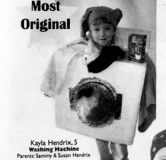 Small child wearing a washing machine costume complete with clothes around their face and a box of laundry detergent.