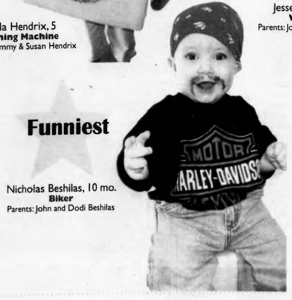 Baby with a drawn on mustache wearing a Harley Davidson shirt, jeans, and a bandana on their head.