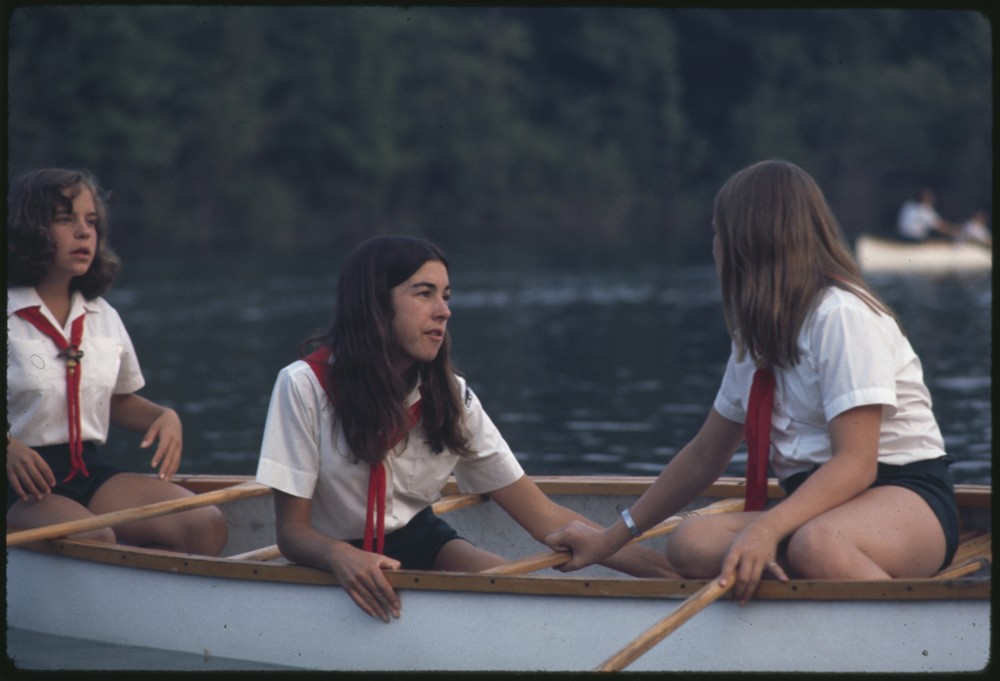 Three individuals in uniforms witting in a canoe on a lake.