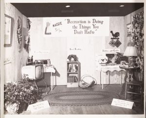Black and White photograph with dispalys of recreation activities for women like canned food items, a bookshelf, gardening and crafting supplies. 