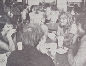 A black-and-white photo of students talking across a lunch table