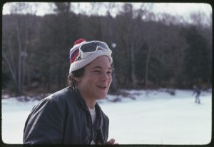 Individual wearing a winter hat and skiing glasses smiling.