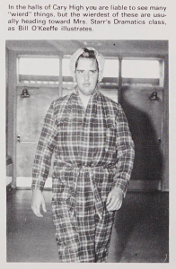 A student in a plaid bathrobe standing in front of a garage door. They have a single curler in the front of their hair.