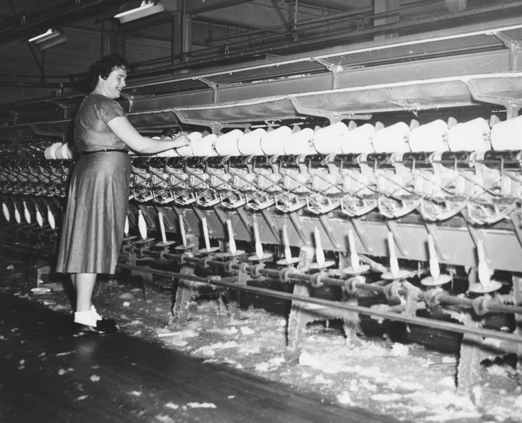 An adult tending to a large piece of machinery in a fabric mill.