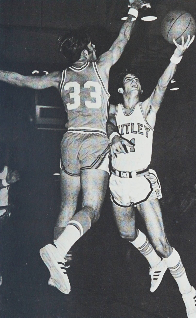 A black-and-white photo of two student basketball players on the men's team jumping in the air and reaching for a basketball.