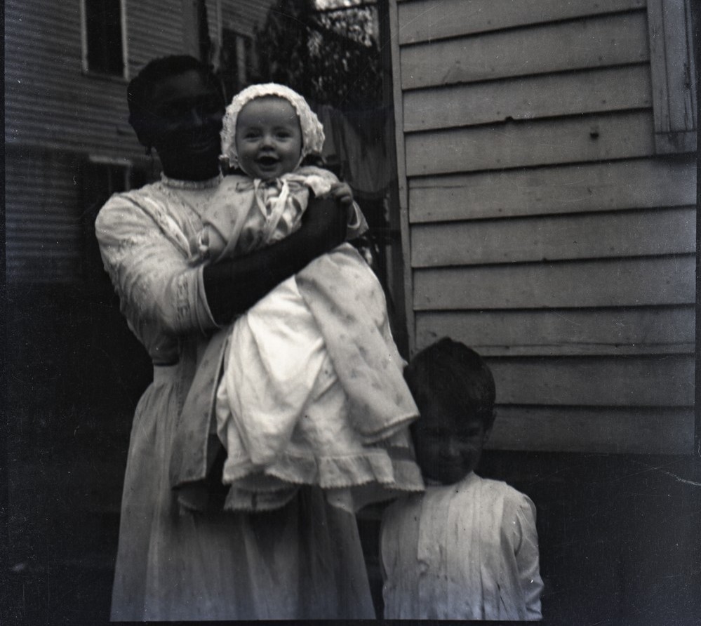 Individual holding a baby in their arms. Standing next to them is a small child.