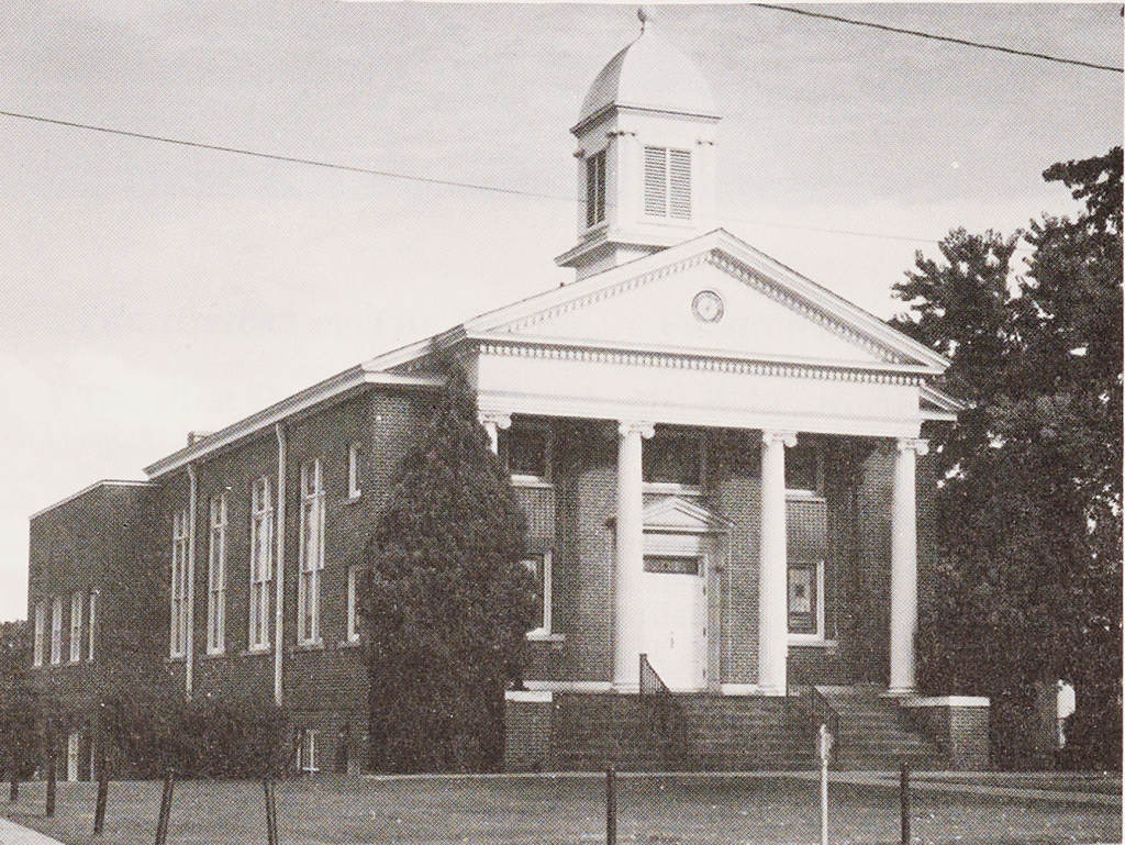A black-and-white photo of First Presbyterian Church of Mount Holly. The church building is primarily brick with a set of white columns at the front entrance.