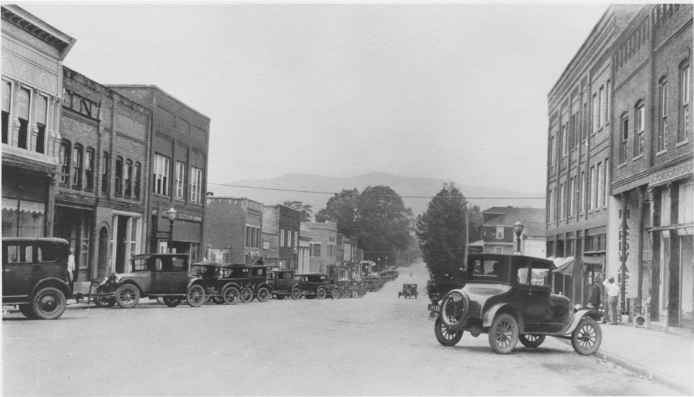 A view of Brevard's West Main Street in 1925. Lining either side of the street are  two-story brick buildings and cars that resemble Model Ts. 