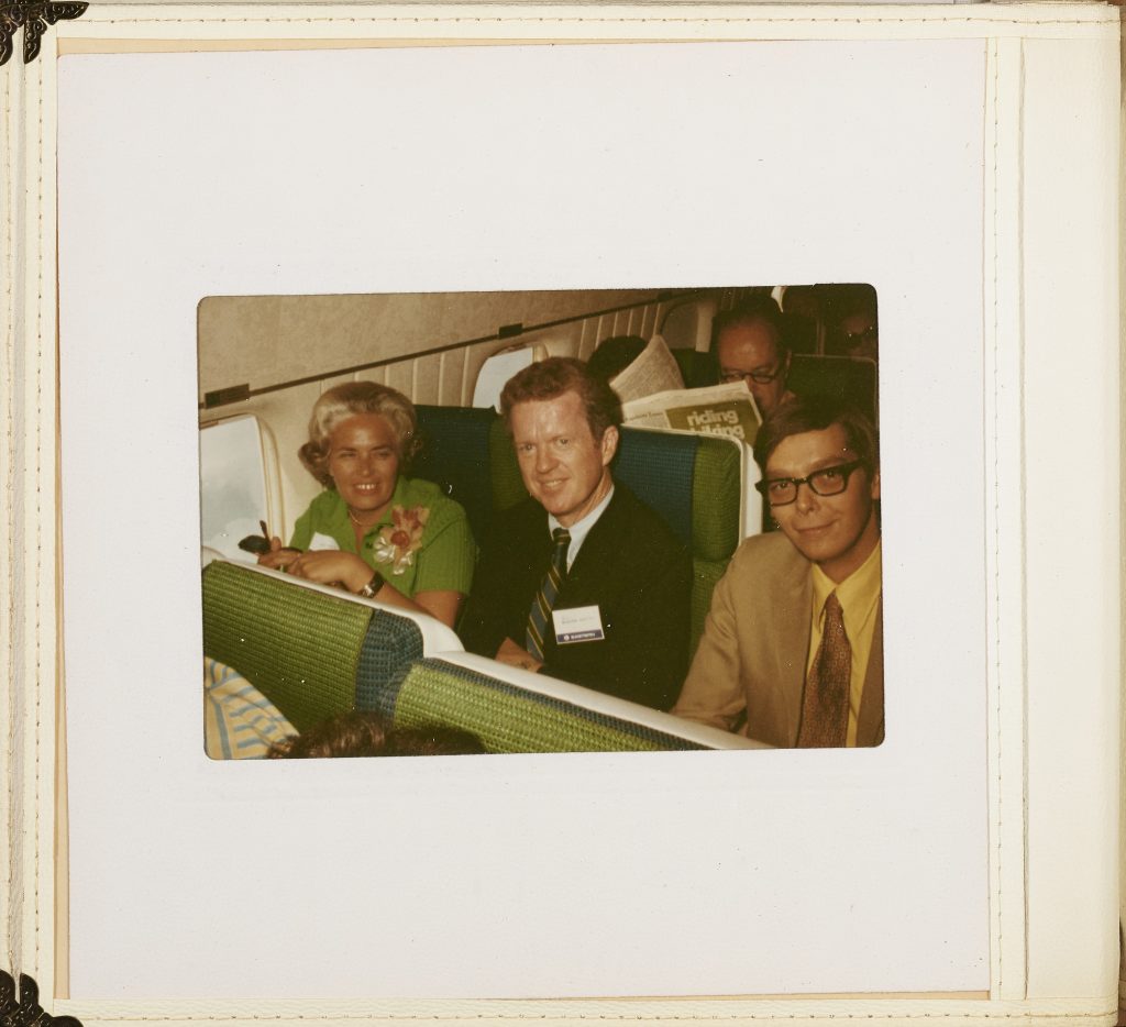 Three adults looking at the camera in a row on an airplane