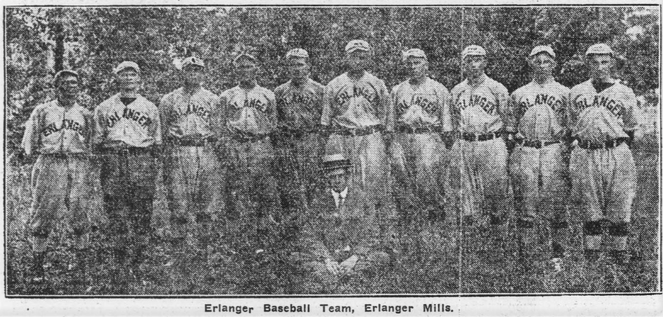 Ten men in 1917 style baseball uniforms standing in a row with their coach, in a suit and hat, kneeling in front
