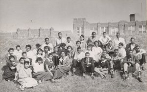 photograph of students sitting on a hill in front of a school building