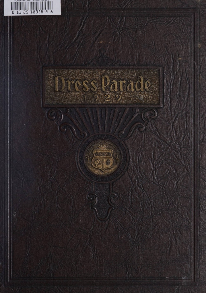 A brown, leathery yearbook cover with a brass coat of arms in the middle. Also on a brass plate are the words, "Dress Parade 1929."