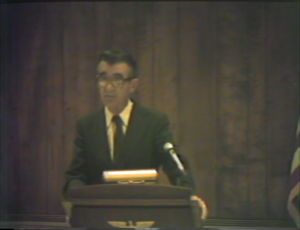 A white man wearing a suit and tie and standing at a podium with a microphone.