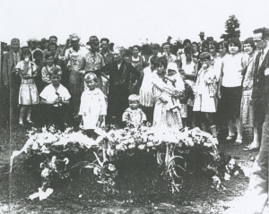 A black-and-white photograph of many adults and children gathered around a coffin.