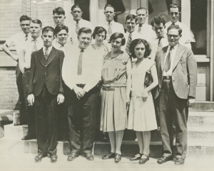 A group portrait of fifteen adults standing together on steps in front of a building.