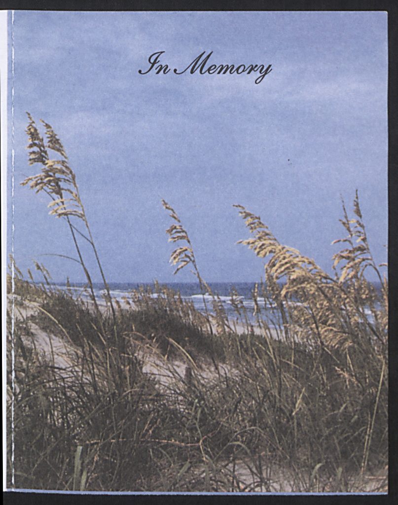 The front of a prayer card with a color photo of the beach and the words "In Memory" written in cursive.