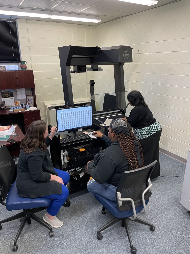 Staff members gather around a computer and overhead scanner