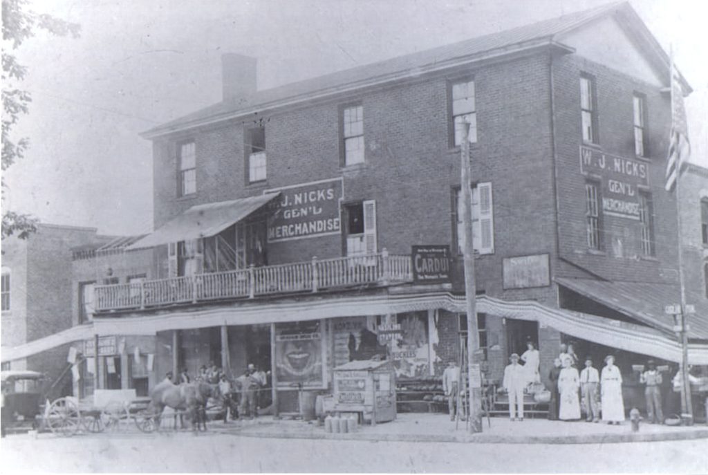 Photograph of the outside of the W. J. Nicks store from 1915. There are people standing outside along the sidewalk including a horse and buggy.