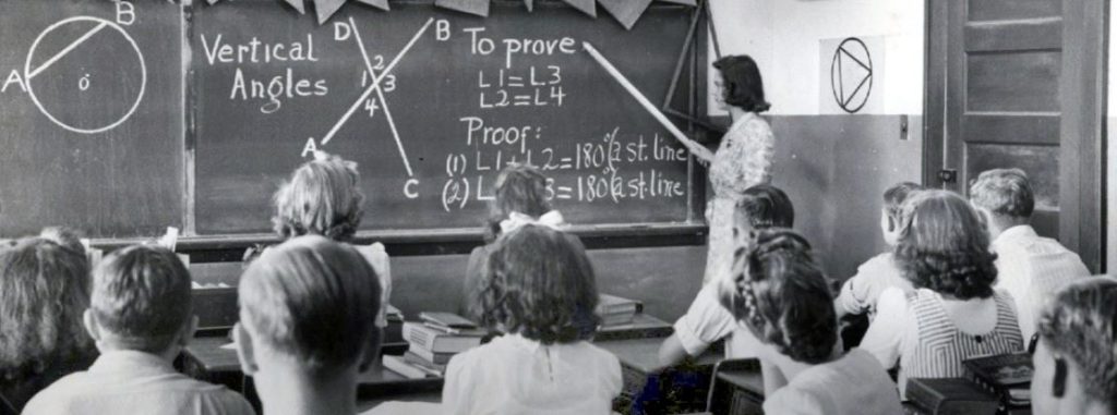 Students in a classroom watch as a teacher indicates geometry lesson on a charkboard