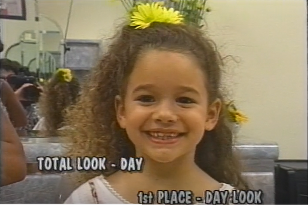 Individual posed with styled hair featuring two yellow flowers. At the bottom of the image is written: "Total look - day. 1st place - day look."