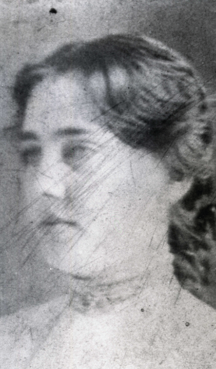Image of a woman looking off into the distance. She is wearing a garment with a high neckline with her hair styled out of her face.