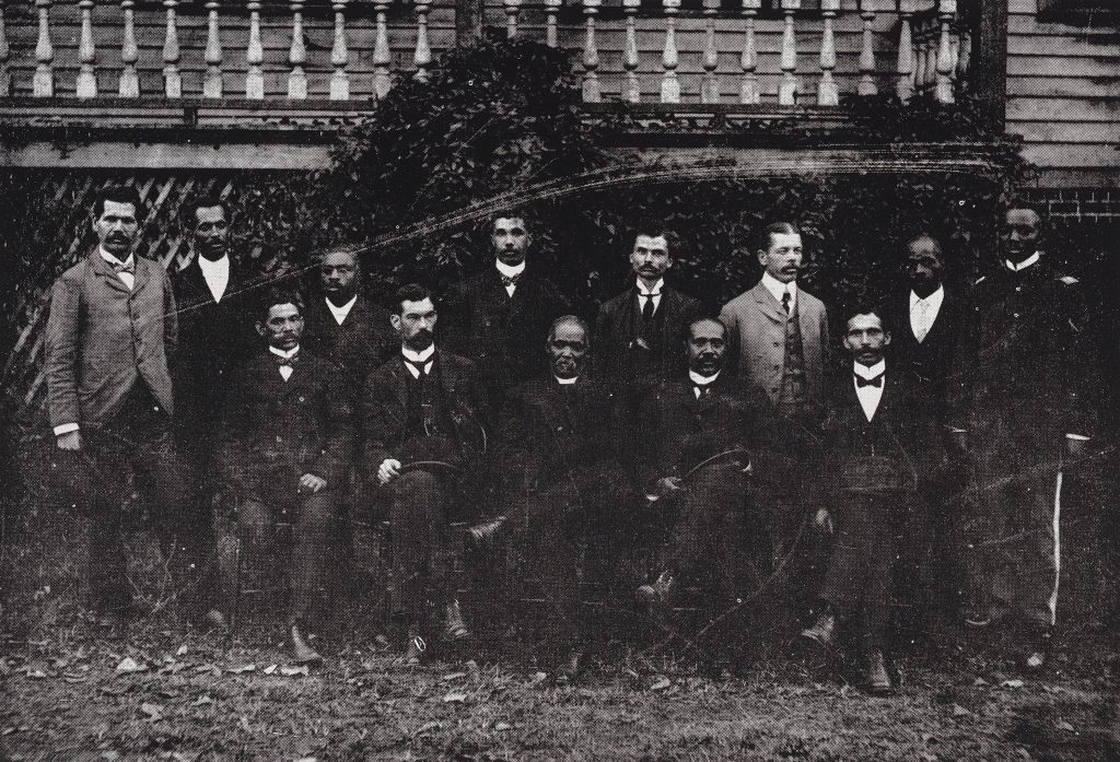Two rows of individuals posed in suits. The back row is standing while the front is sitting.