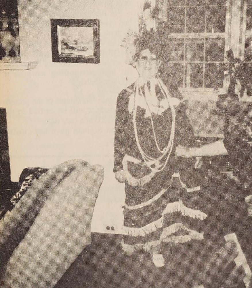 Individual dressed as a flapper, with long pearl necklaces, hair piece, and long dress with fringe.