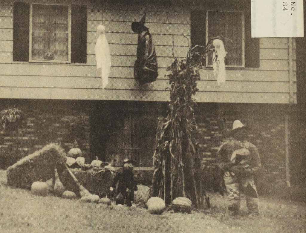 House featuring Halloween decorations in the yard including ghosts and witches suspended from the roof, haybales, pumpkin man, pumpkins, and corn stalks.