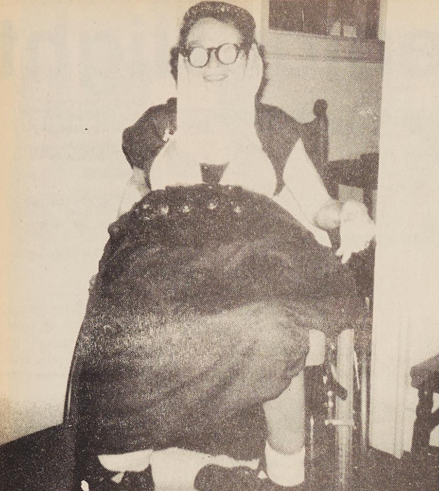 Individual in a wheelchair with glasses dressed as a belly dancer.
