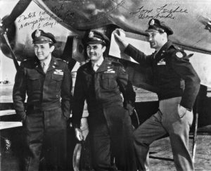 Three men in 1940s military uniforms pose in front of an aircraft.